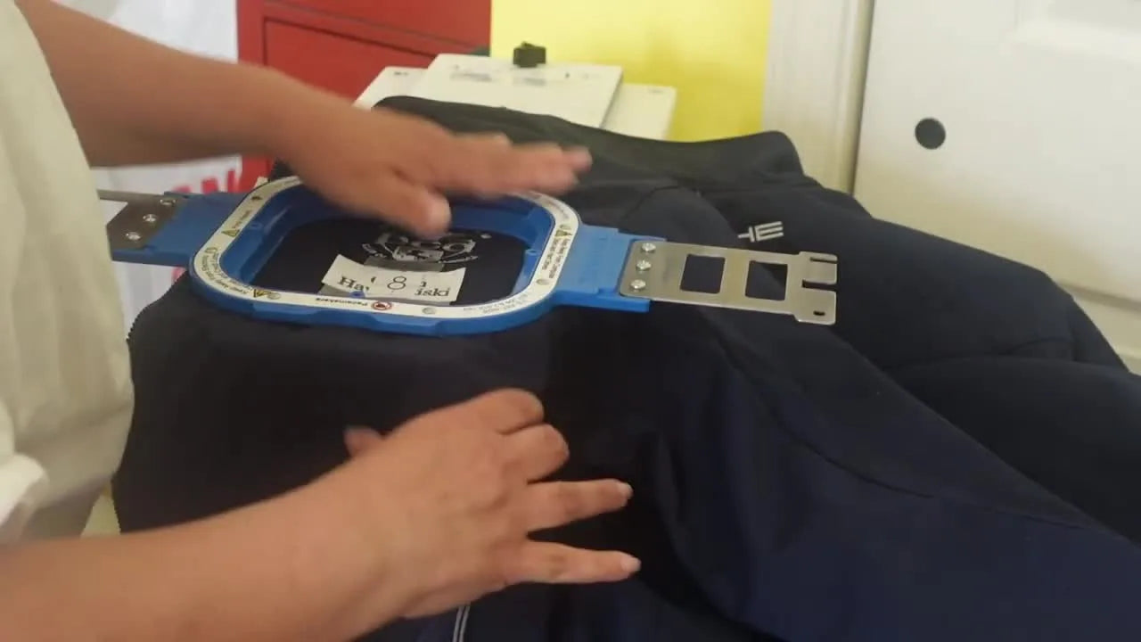 A blue magnetic hoop snaps onto a softshell jacket on a hooping station, showing how bulky garments can be secured quickly and evenly.