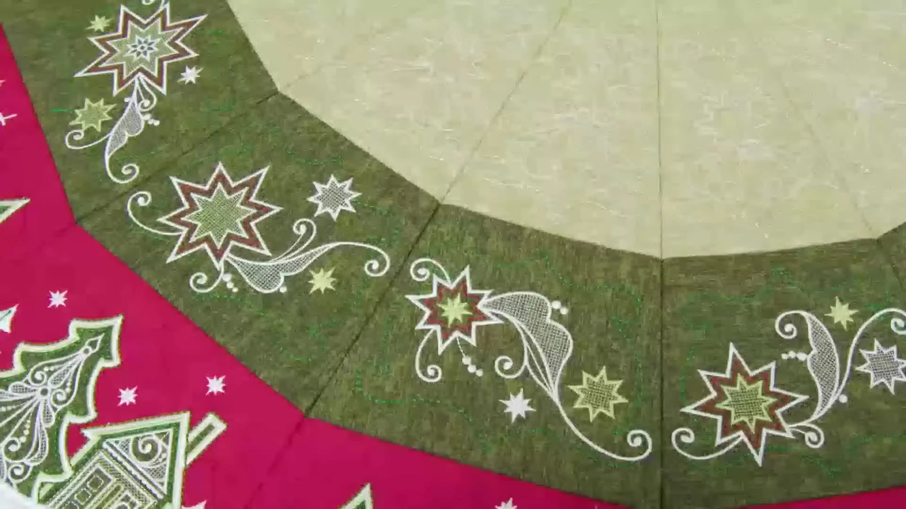 A finished Evergreen Star Christmas tree skirt displayed under a Christmas tree, showing the red-and-green tiled embroidery scene.