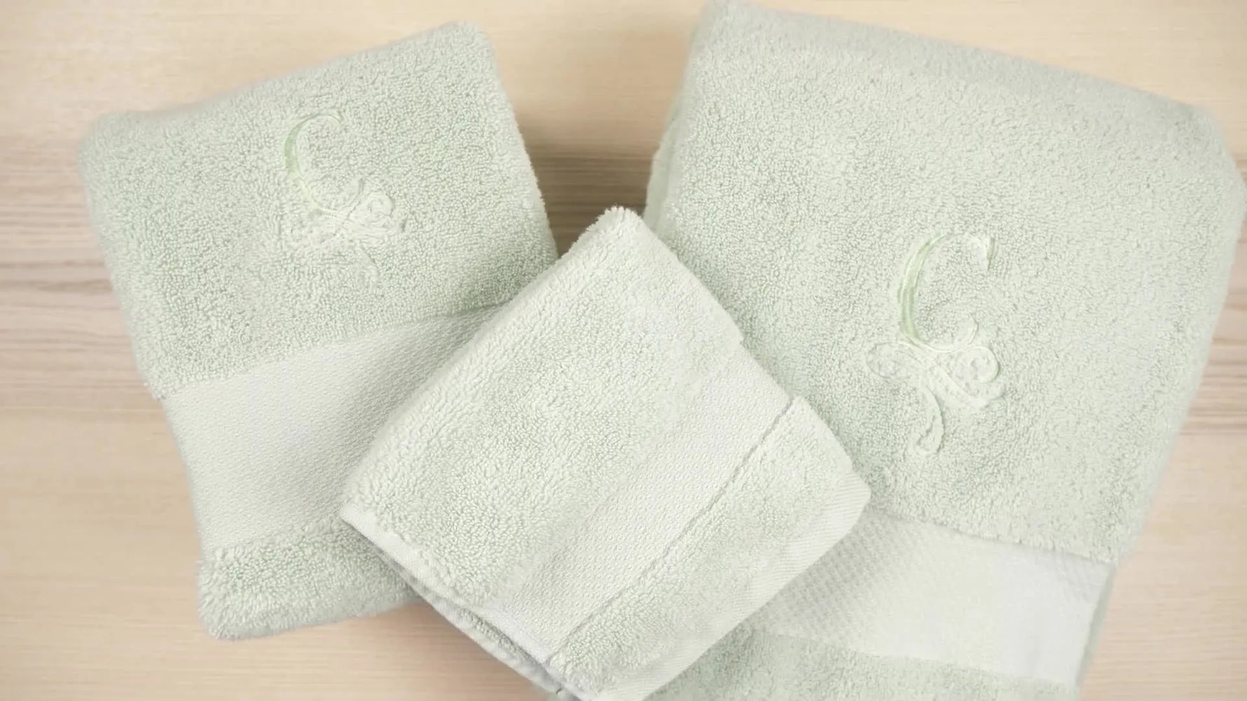 A neatly folded set of plush green towels with a clean, high-end monogram finish that doesn’t disappear into the terry pile.