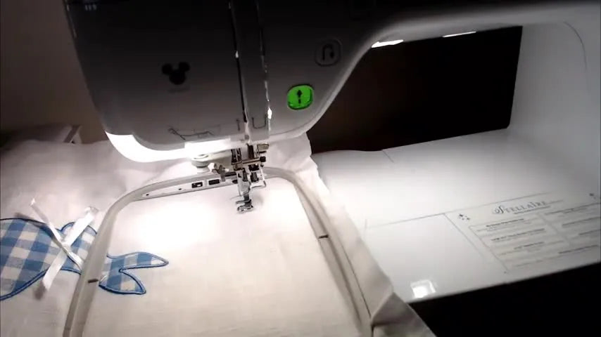 A close-up of the Brother Stellaire actively stitching the first letter on a hooped towel, showing real-time embroidery in progress.