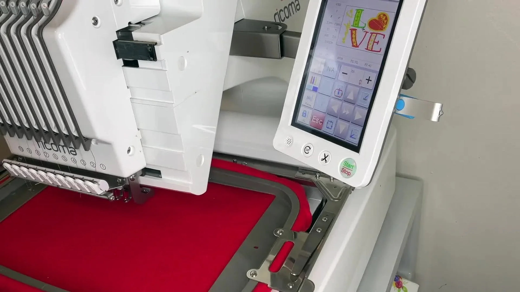 A close-up of the Ricoma EM1010 needle stitching a pink heart on a red sweatshirt during the main run.