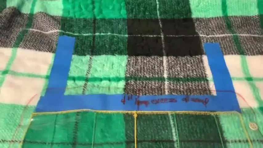 A close-up of a quilt with a bold blue painter’s tape line marking the edge of the previous stippling row for precise re-hooping alignment.