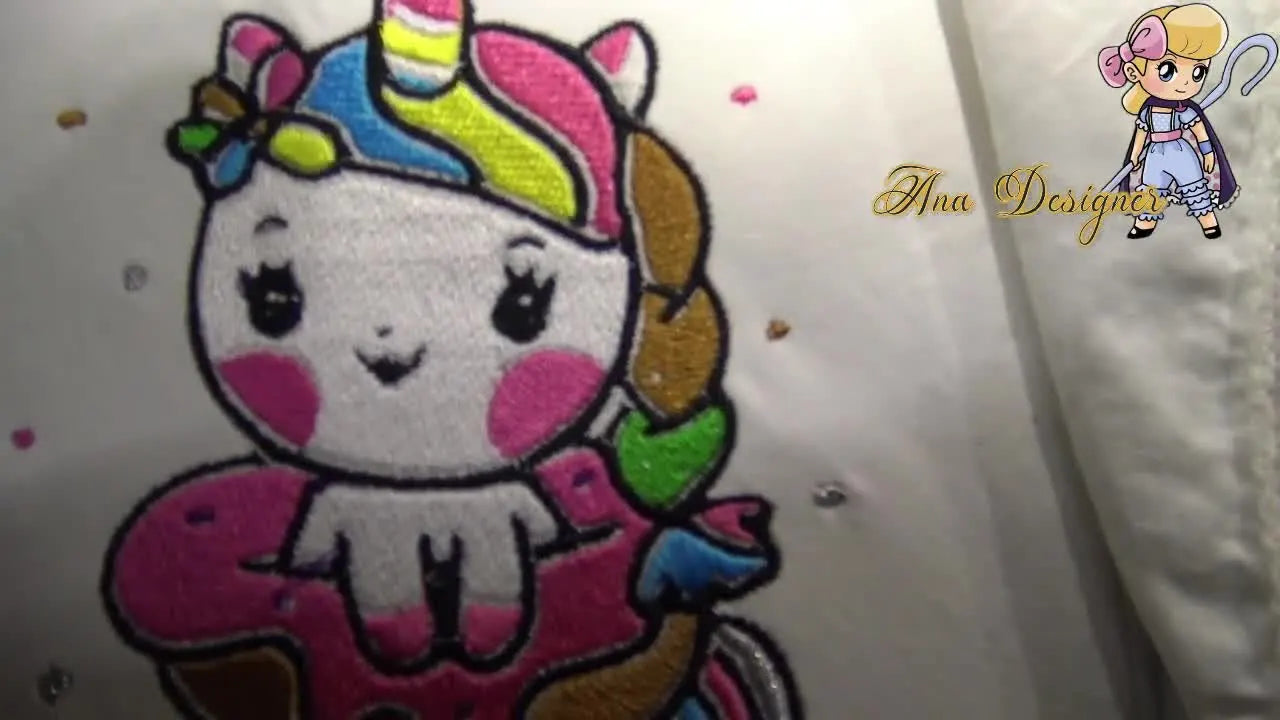 A finished unicorn sitting in a pink donut stitched cleanly on white lace-trimmed fabric, showing crisp black outlines and smooth fills.