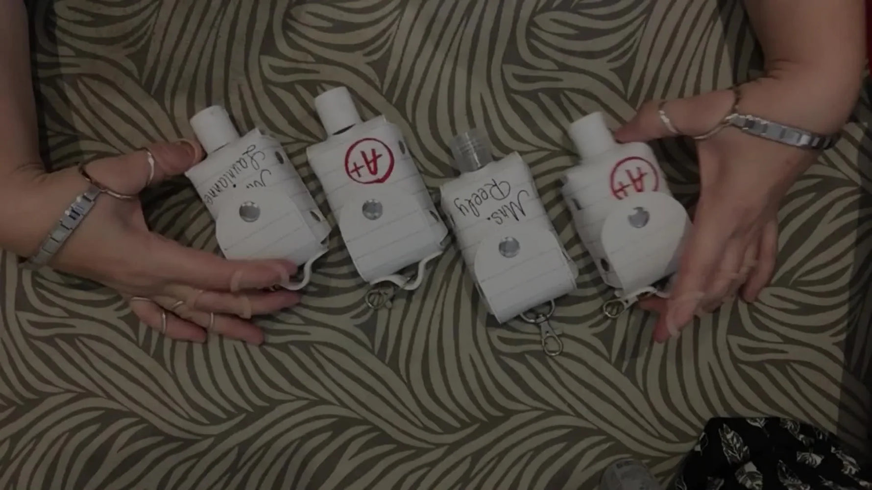 Four finished white vinyl ITH hand sanitizer holders with different text options displayed with 2 oz bottles.