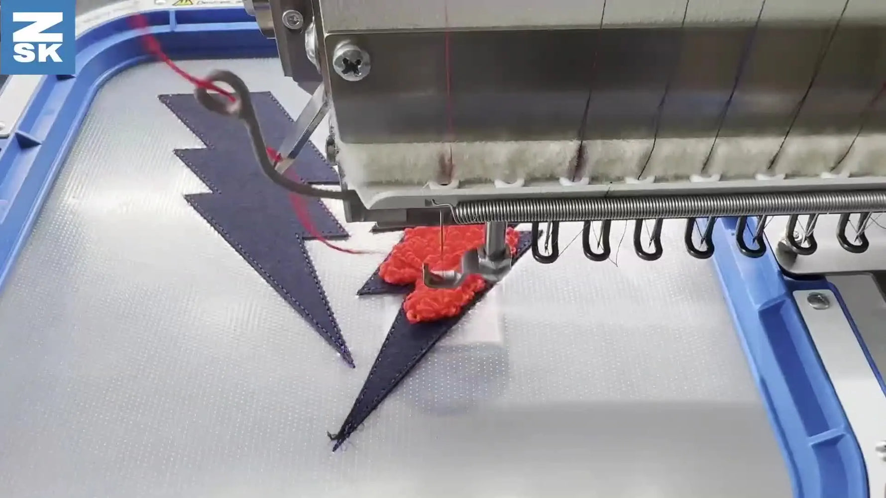 A close-up of a ZSK embroidery machine stitching tall red faux-chenille loops on black fabric held in a blue magnetic hoop.