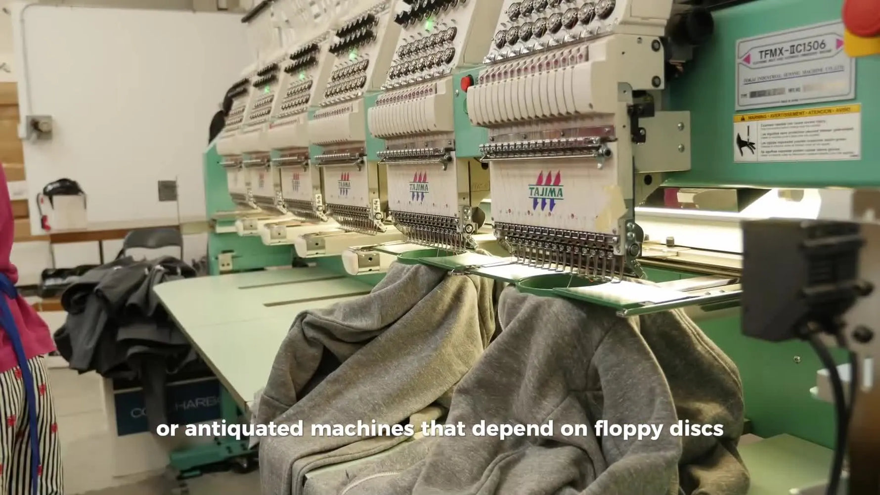 A line of Tajima commercial embroidery heads running in production on hooped garments, showing what “real operational proof” looks like.