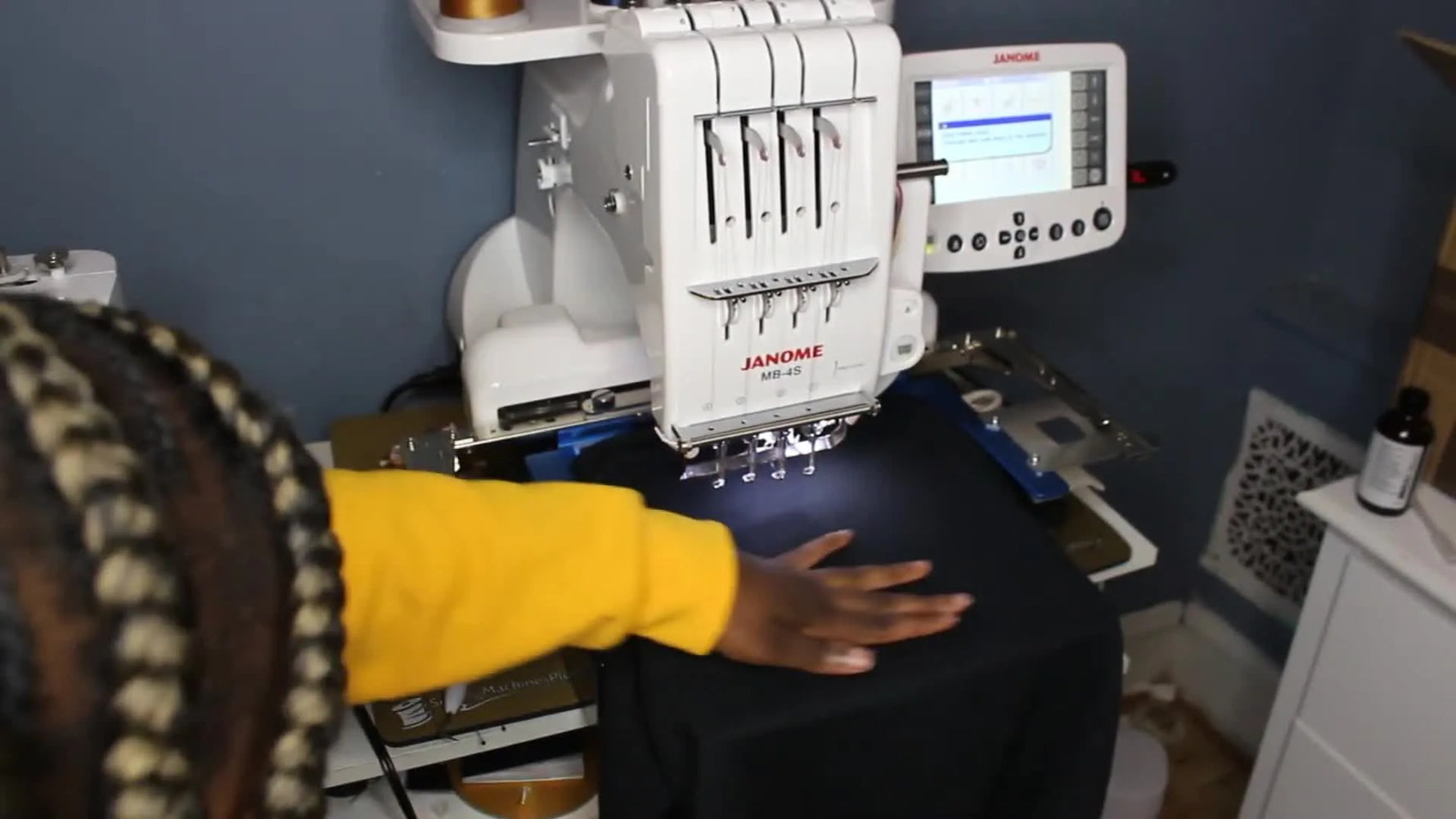 Hands smooth a black sweatshirt onto sticky stabilizer on an EZ Frame, creating a flat stitch field without a traditional top hoop.