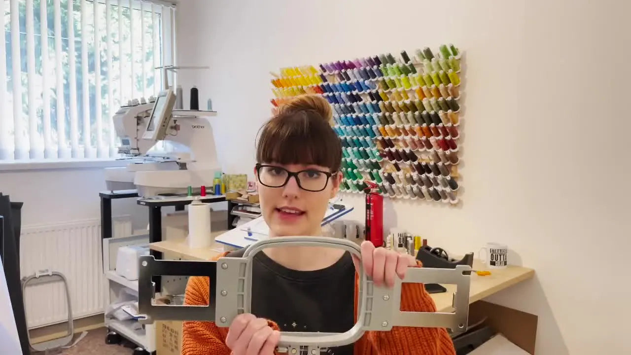 Lauren holds a standard grey plastic embroidery hoop while explaining why sewing-field size can make or break a beginner’s first machine choice.