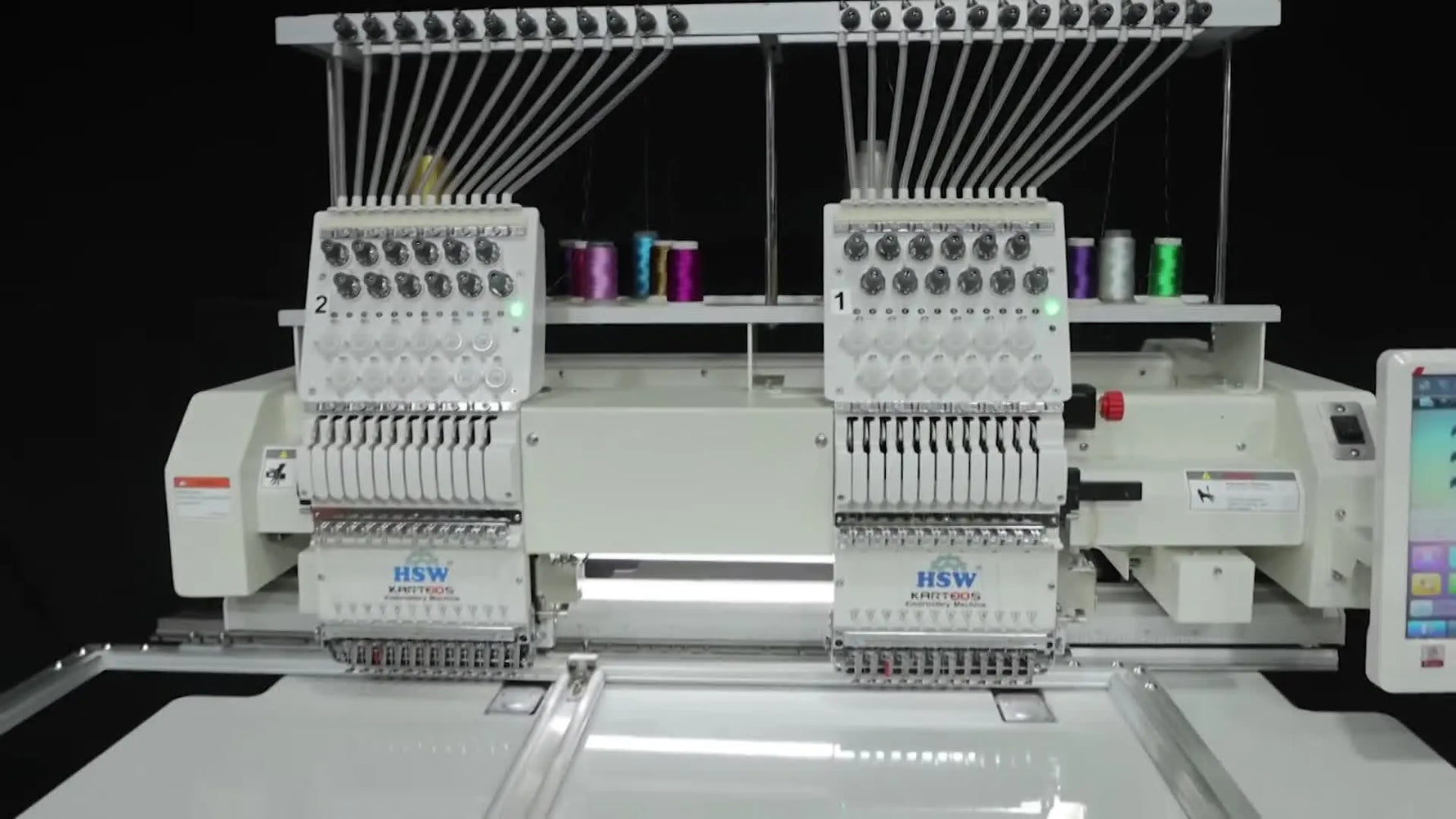 A wide shot of the HSW two-head embroidery machine running a large border design on an aluminum sash frame across a white table.