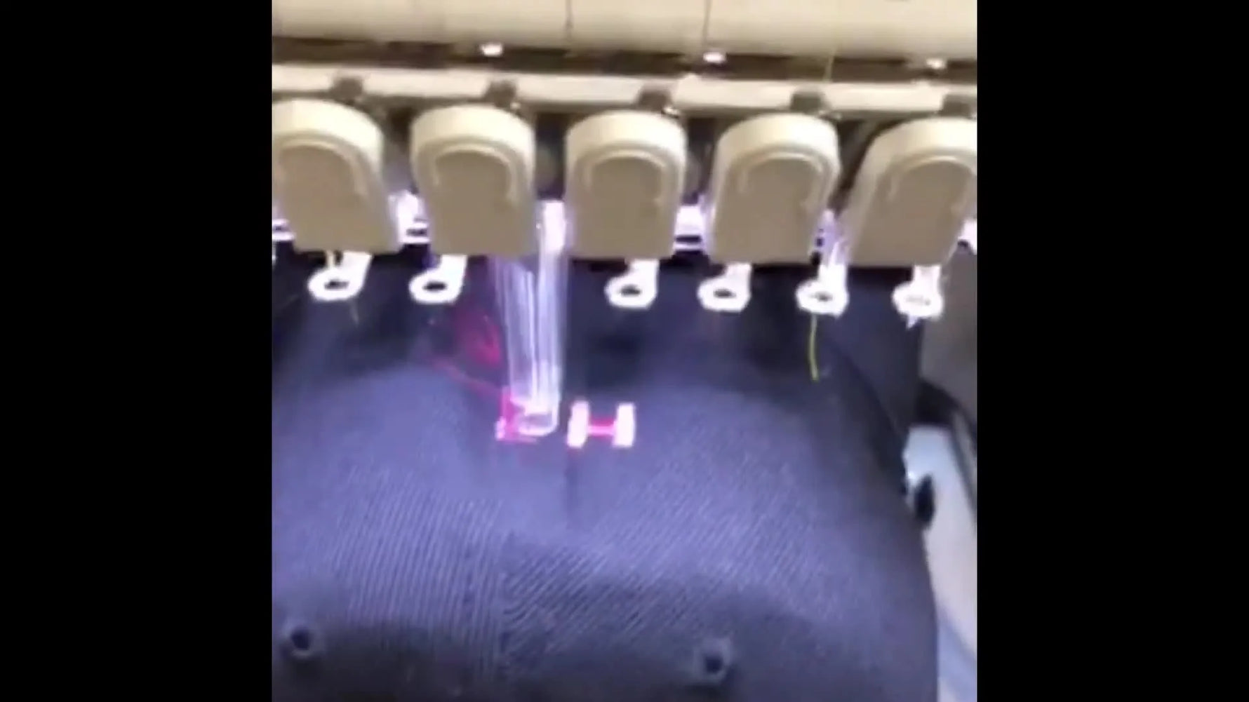 A close-up of a Ricoma multi-needle machine stitching a purple letter on a black cap during an active cap embroidery run.