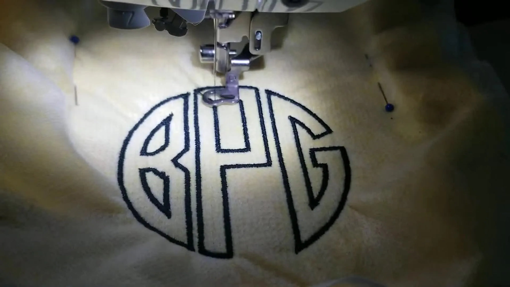 A finished three-letter satin monogram (BPG) displayed flat on a yellow textured towel.