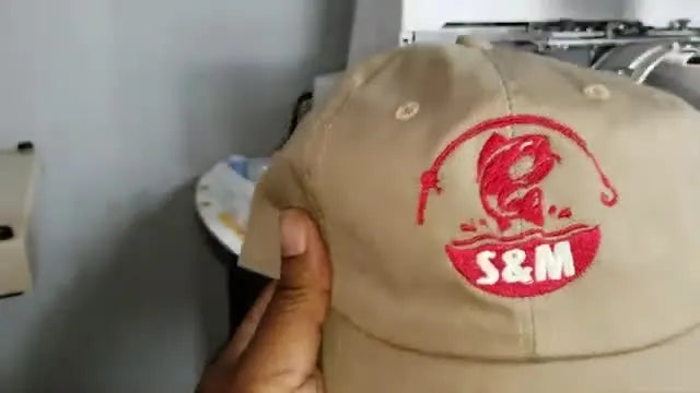 Close-up of a finished tan unstructured dad hat showing a clean red-and-white fishing logo centered on the front panel.
