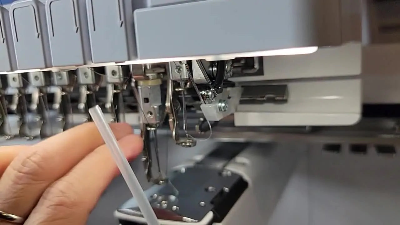 A close-up shows a precise drop of oil being applied to the white felt pad on the Brother PR1055X needle bar assembly.