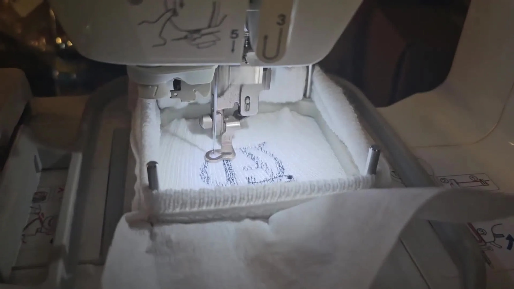 A close-up action shot of a Brother embroidery machine stitching a black logo onto a white ribbed sock held in a 2x2 metal sock hoop.