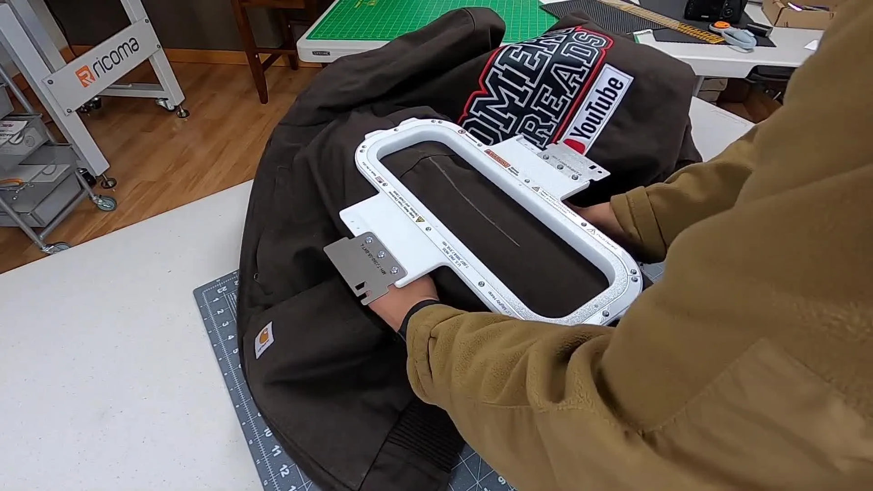 A top magnetic frame is pressed onto a Carhartt jacket sleeve on a freestyle hooping station, aligned to a chalk centerline for a straight sleeve embroidery placement.