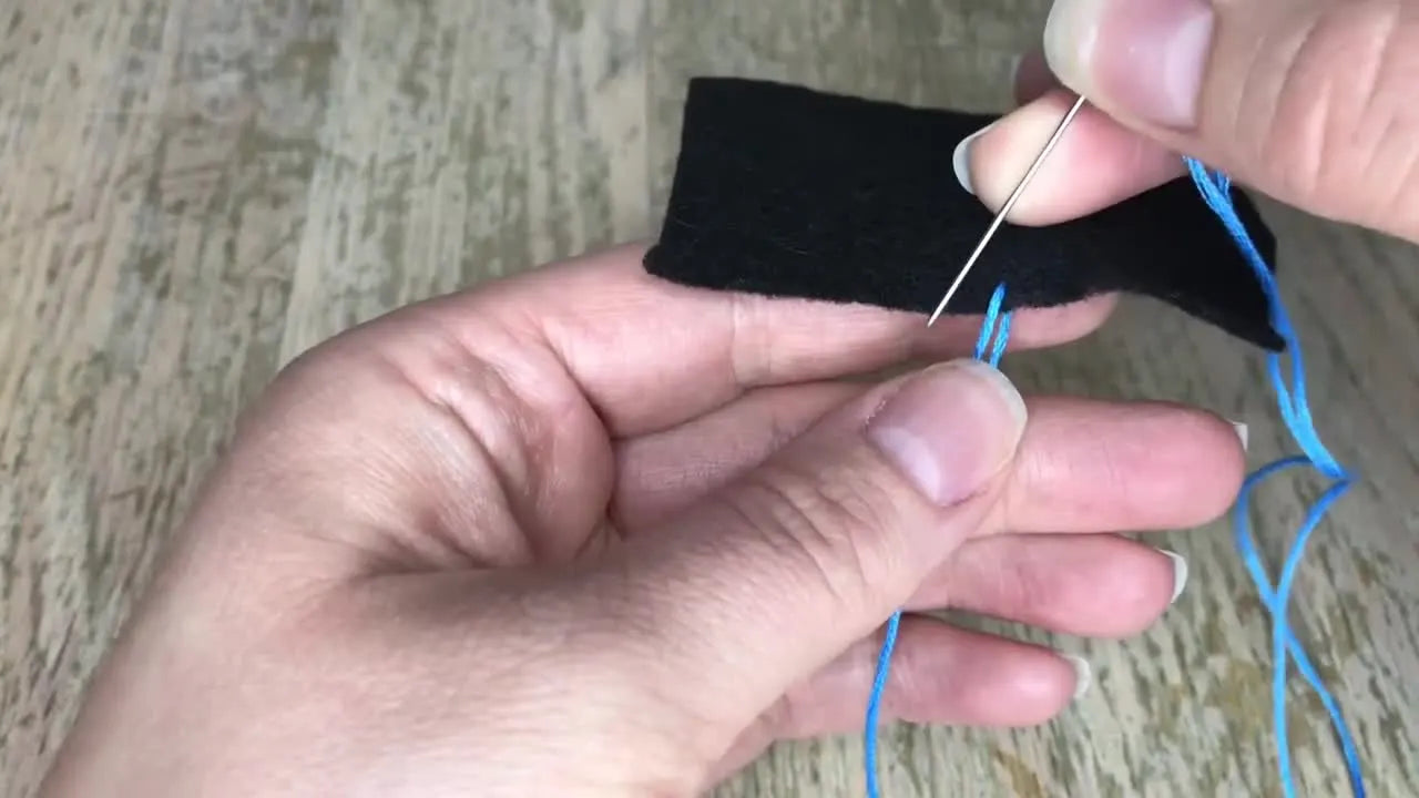 Needle passing behind both strands of the blue thread loop to form a knot.