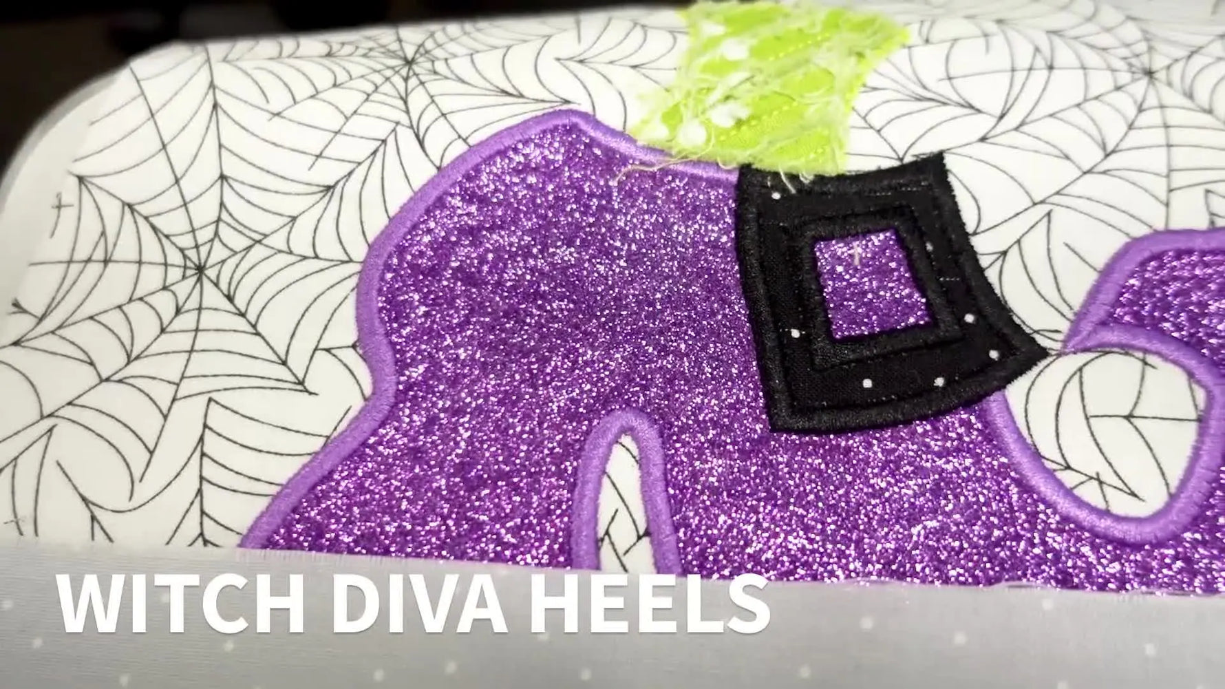 Extreme close-up of a purple glitter Mylar appliqué witch shoe showing a clean satin-stitch edge and reflective texture.