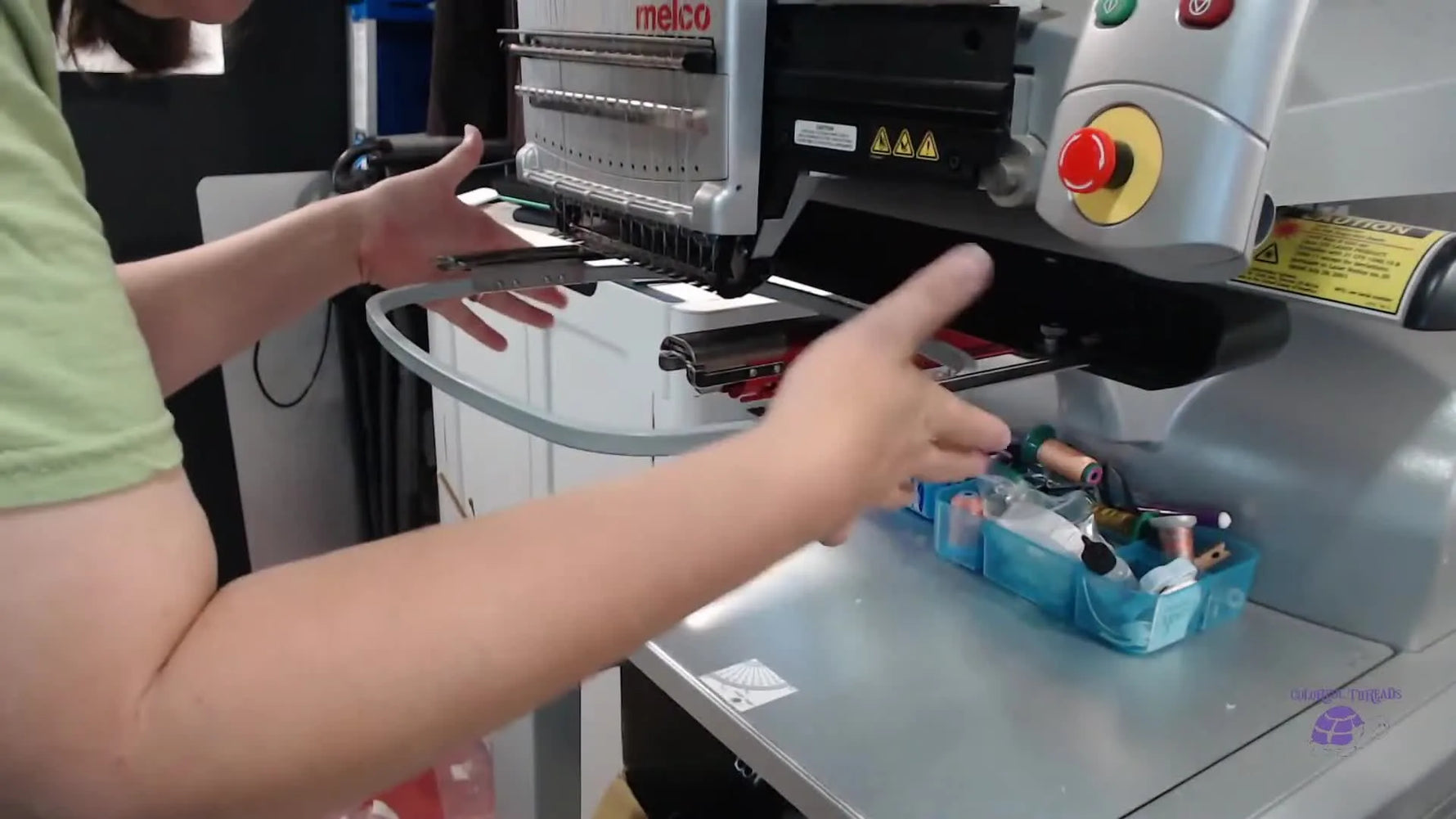Close-up hands squeezing both Melco hoop arms inward against a hoop to remove side-to-side play for cleaner lettering.