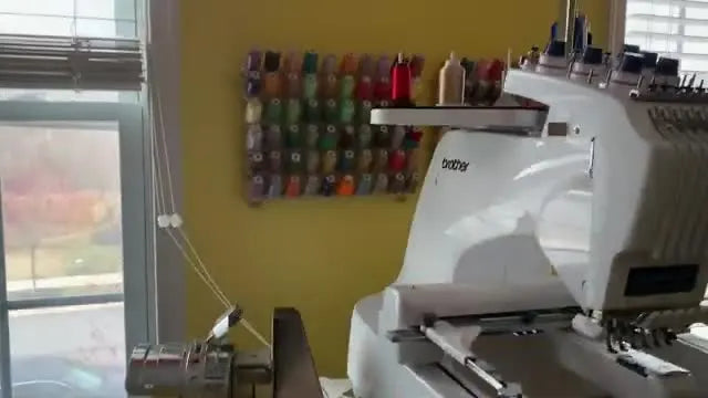 A Brother Entrepreneur Pro X PR1055X 10-needle embroidery machine on its stand, positioned as the main production centerpiece of a compact home studio.