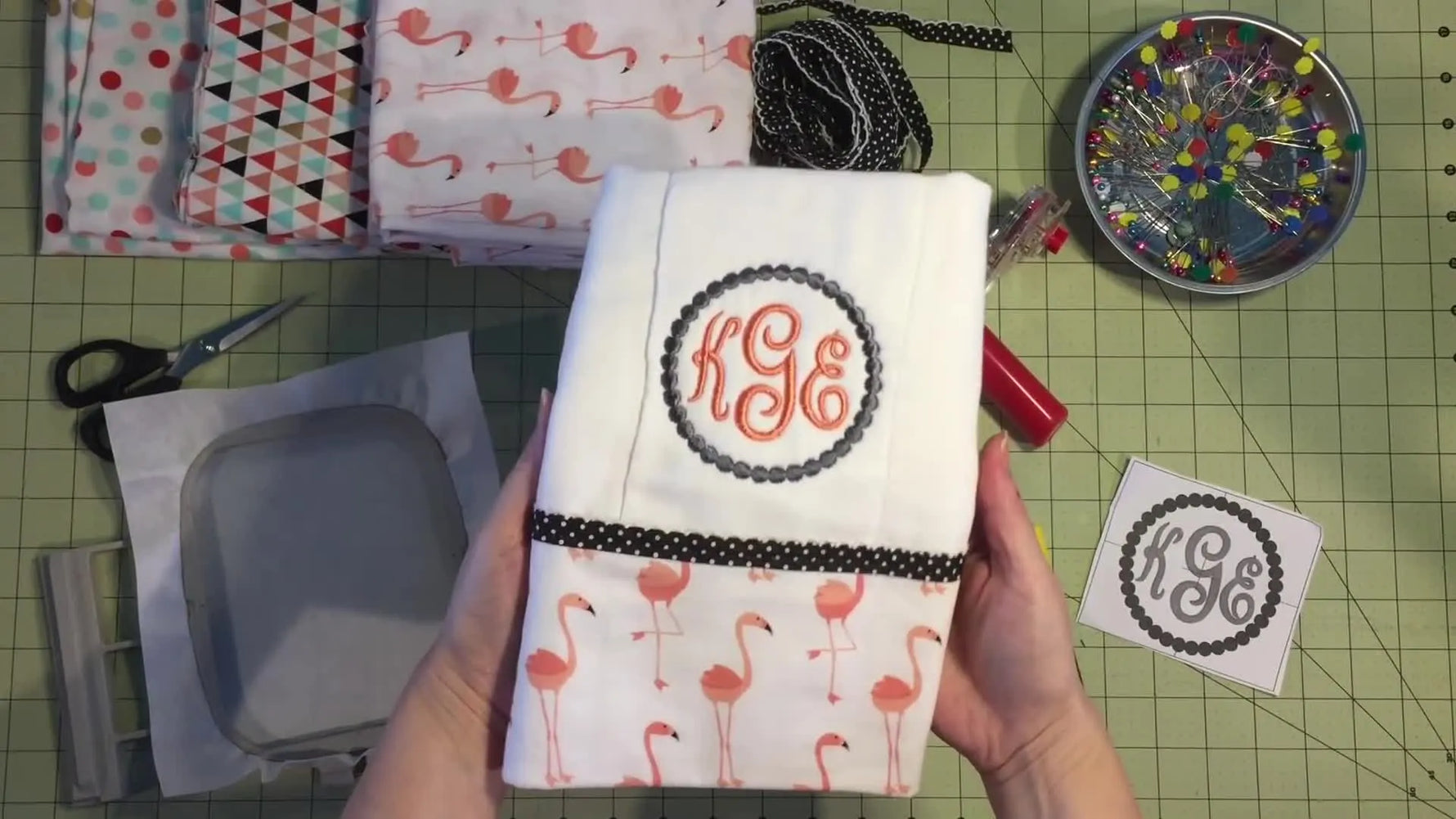 A finished white burp cloth made from a prefold diaper, featuring a flamingo fabric border and a centered embroidered monogram.