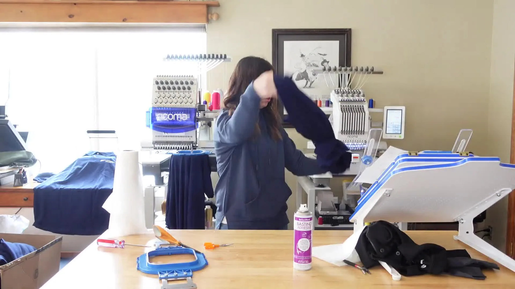 Close-up of a magnetic hoop on an embroidery machine as it stitches a logo onto a blue garment.