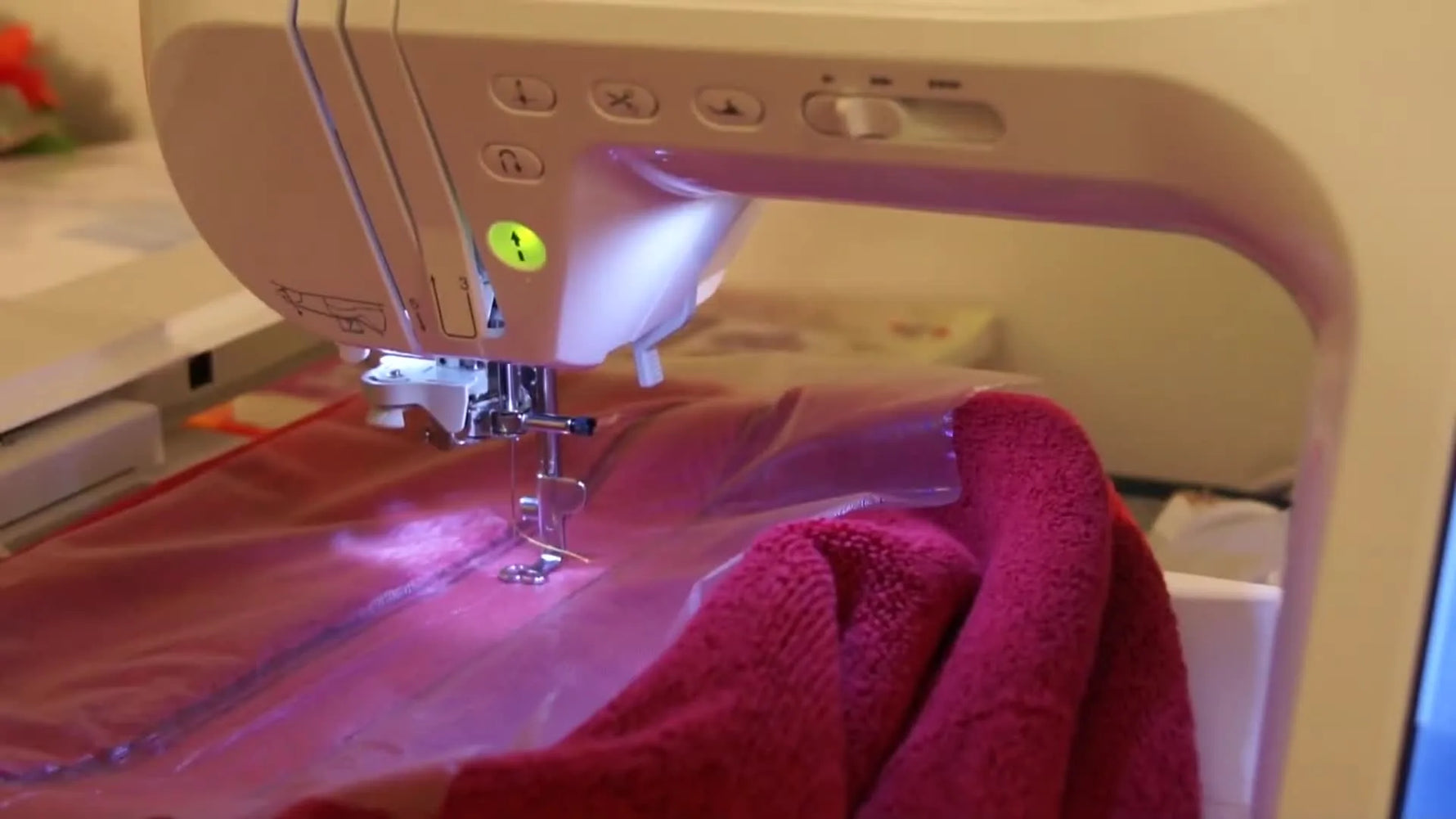 Close-up of the Brother Innov-is 2800D stitching gold text onto a red terry towel through a clear water-soluble topping film.