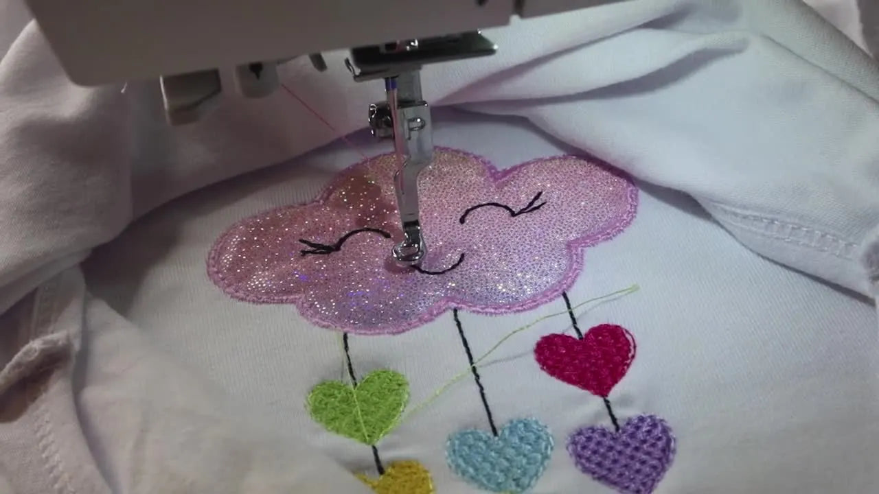 The finished cloud-and-hearts appliqué is shown cleanly stitched on the baby onesie while still in the hoop.