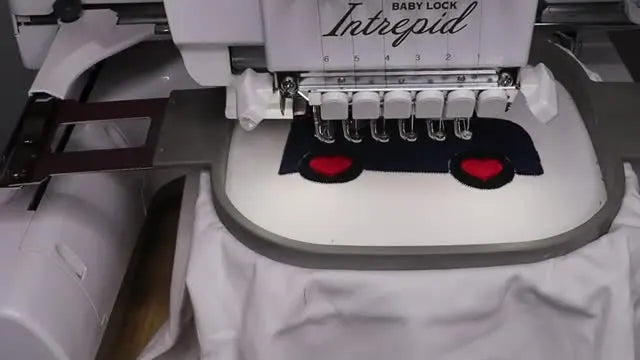 An extreme close-up of the Baby Lock Intrepid running the final satin stitches around red heart appliqué pieces.