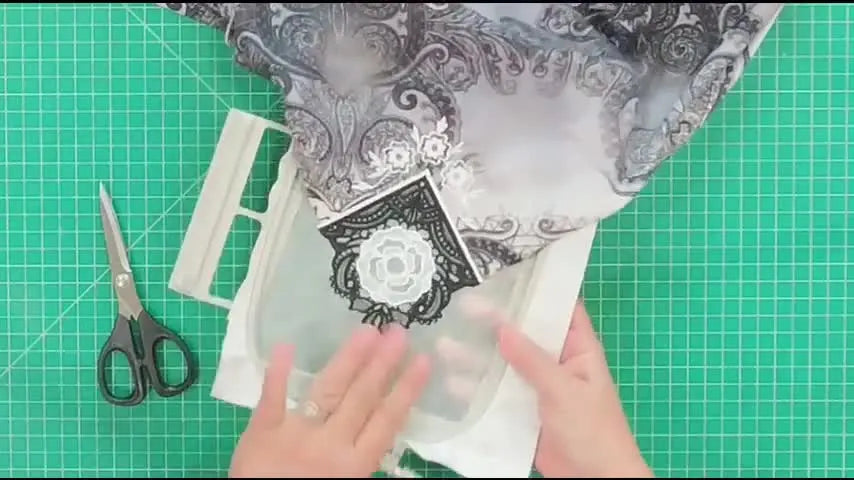 A finished freestanding lace corner stitched into a tunic hem is held up in the hoop for a close inspection of the clean cutwork window and lace density.