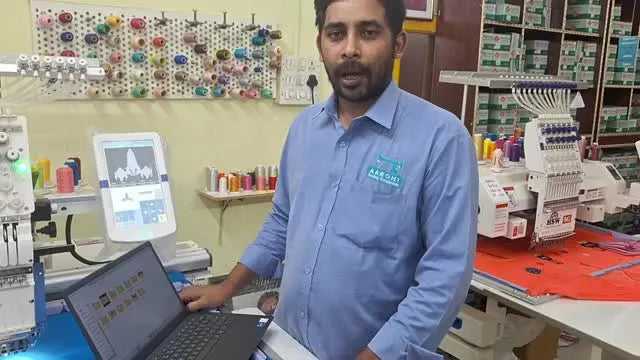 The instructor stands beside a Fortever embroidery machine with a laptop and a wall of thread cones, introducing how to access the free design library.