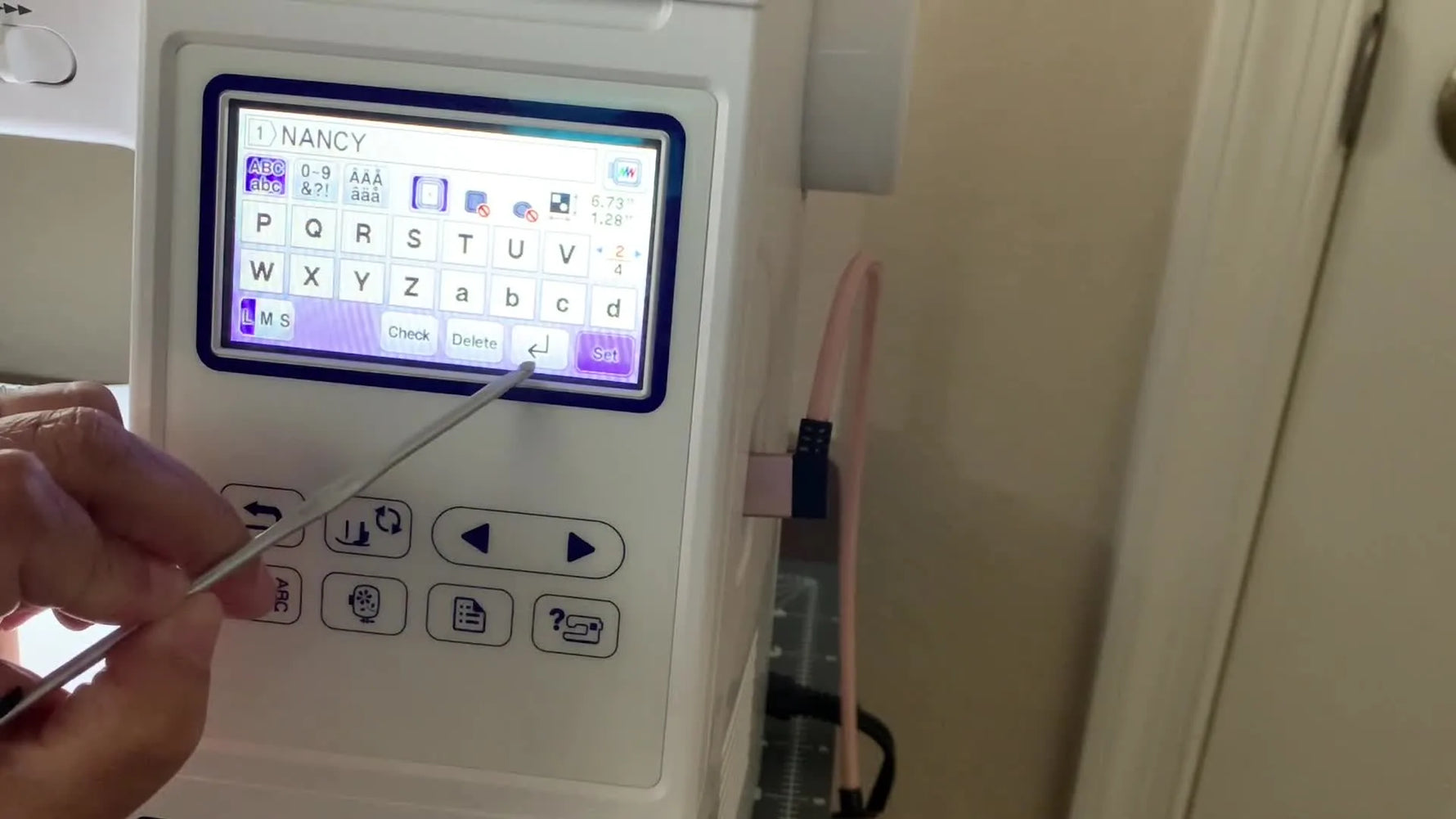 A close-up of the Brother SE1900 screen as a stylus points to the bent-arrow “Next Line / Carriage Return” button used to stack text.