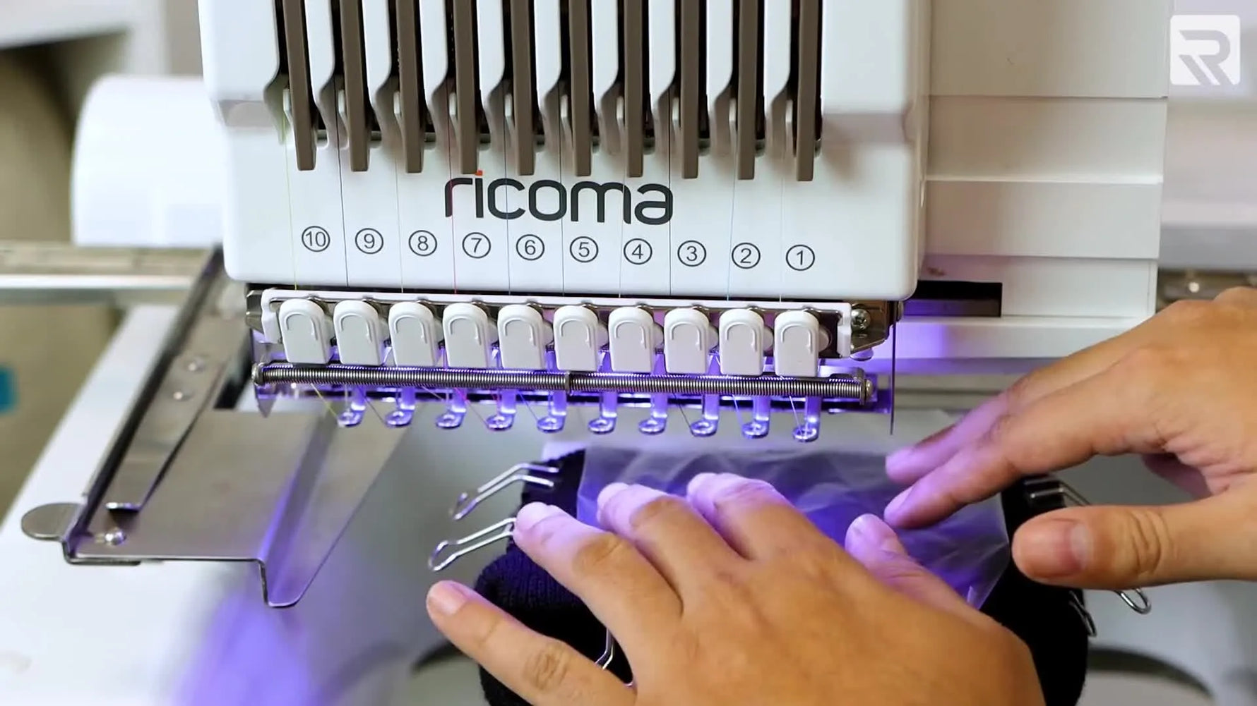 Extreme close-up of the embroidery machine stitching a white outline on a beanie with water-soluble topping in place.