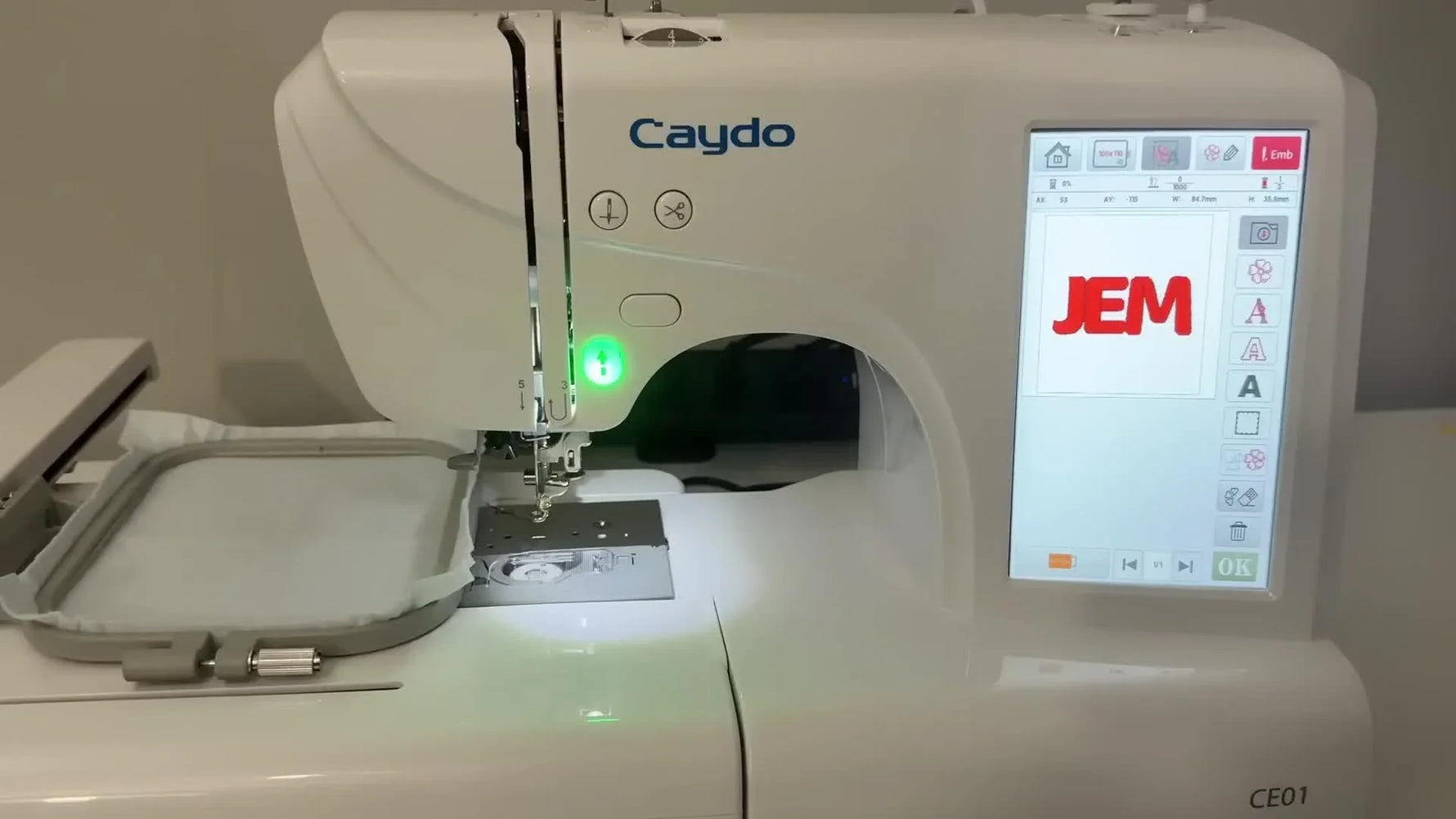 The Caydo CE01 is actively stitching a monogram with the green start light illuminated and the hoop mounted under the machine head.