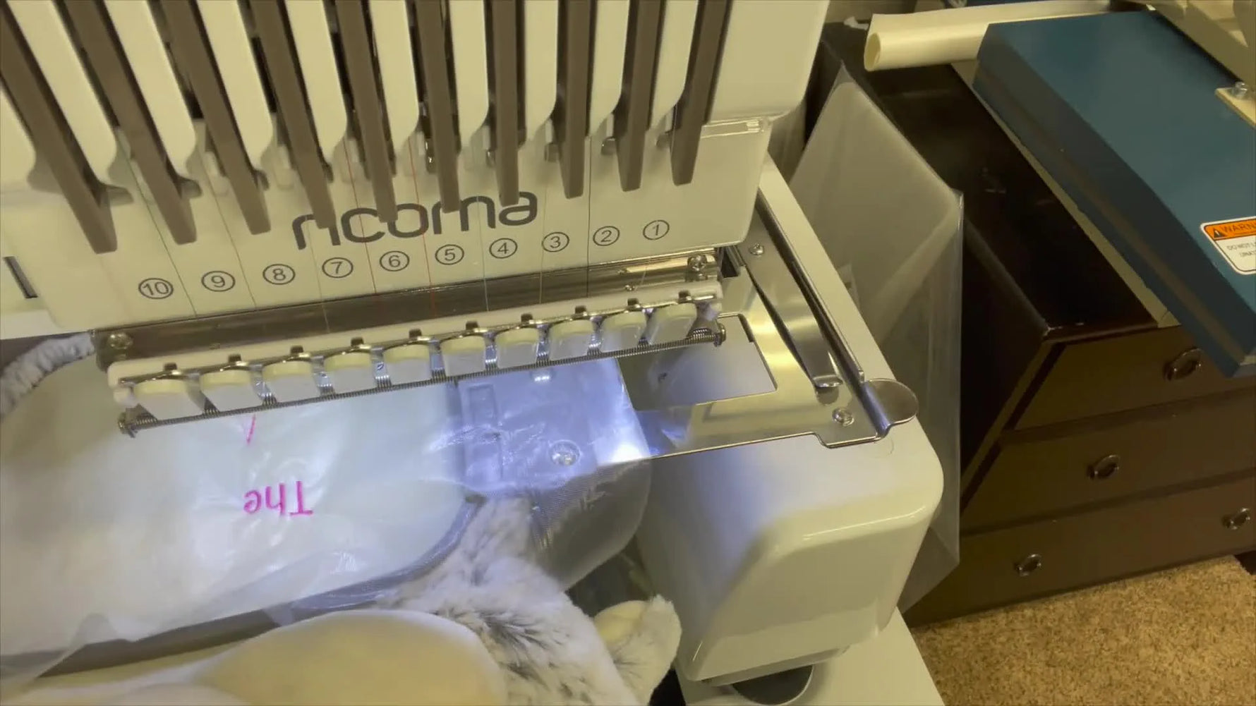 Close-up of the Ricoma EM1010 stitching pink lettering onto the Cubby Buddy bunny’s tummy through a clear water-soluble topper.