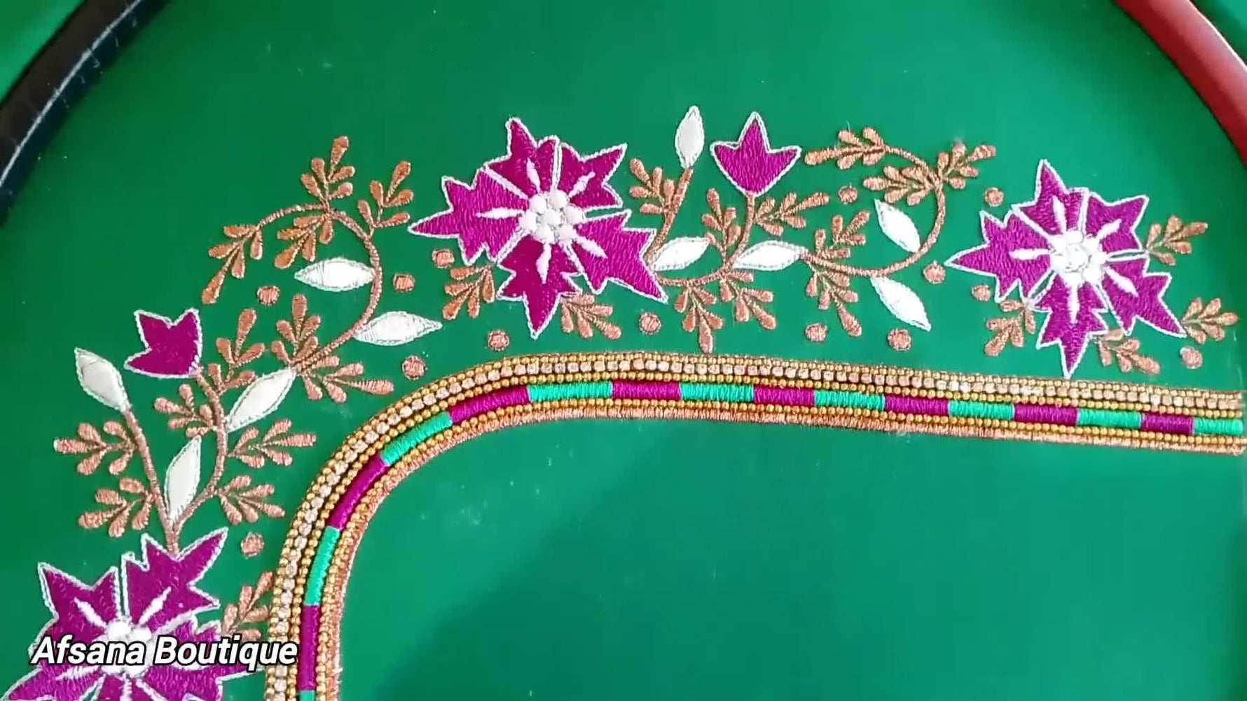 A finished green blouse sleeve piece displayed wide, showing dense purple florals, gold zari vines, and bright white highlights over a curved geometric border.