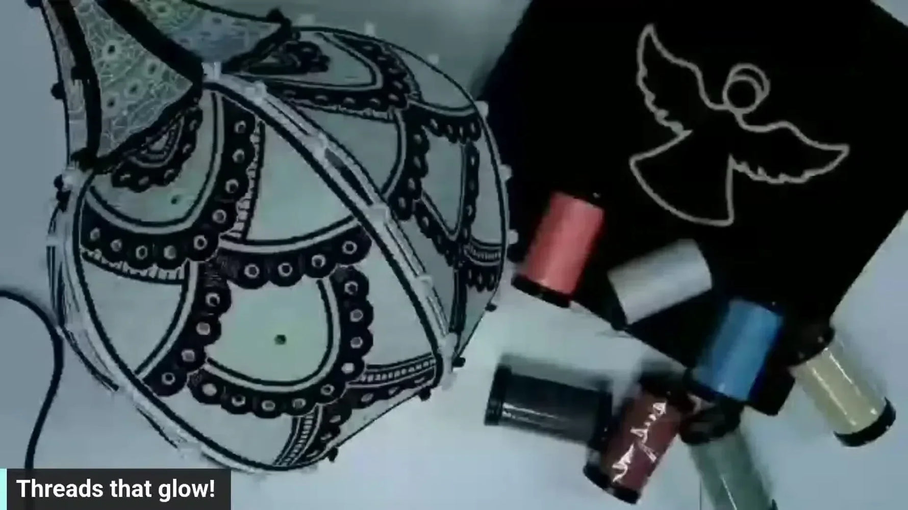 Overhead shot of an embroidered 3D pumpkin and a black fabric swatch with an embroidered angel, surrounded by spools of glow-in-the-dark and reflective threads.