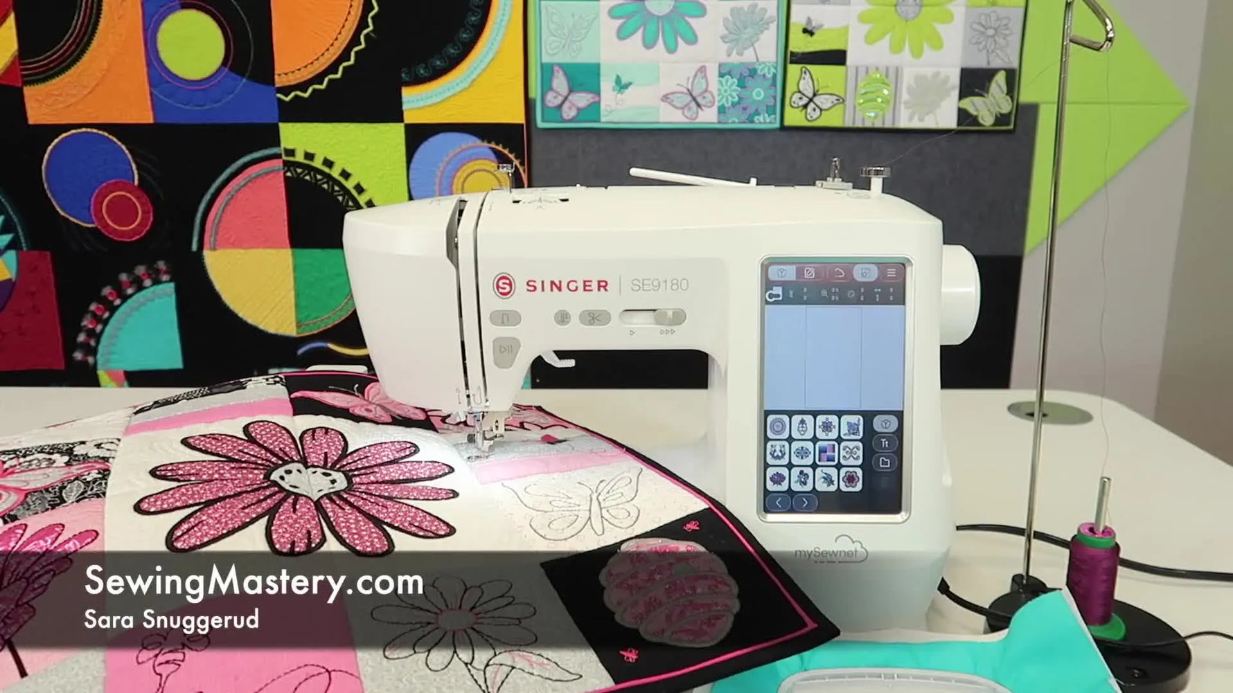 A Singer SE9180 embroidery machine sits ready on a clean table with a colorful quilt backdrop, setting the stage for on-screen design selection and editing.