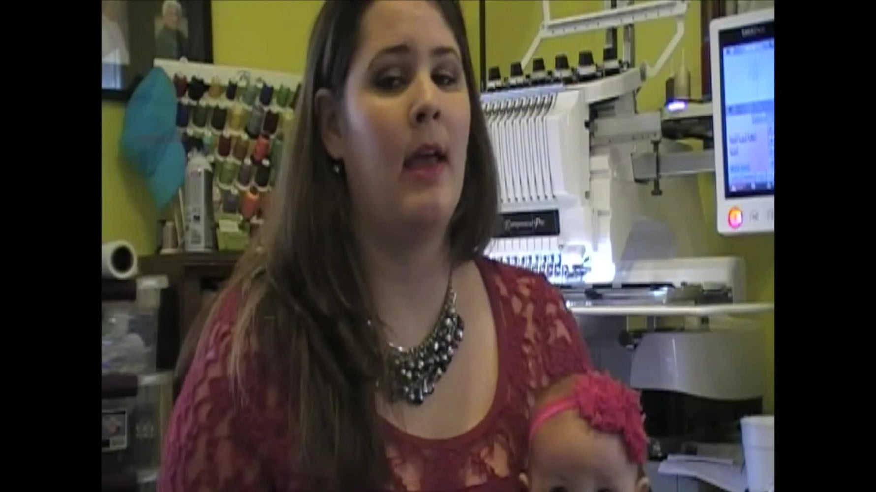 The host gestures toward a 10-needle Brother PR1000e and its thread stand while explaining why multi-needle machines change production speed and hooping options.