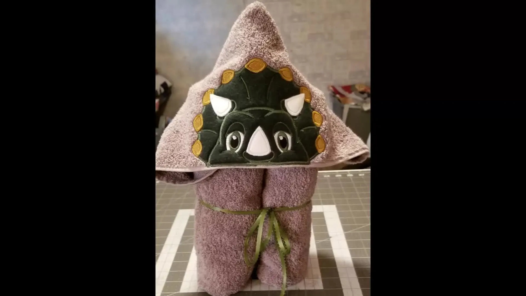 A finished dinosaur hooded towel folded into a gift-ready bundle with the Triceratops face displayed like a character head.