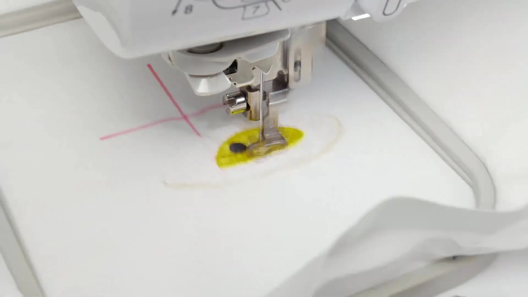 A close-up of the embroidery machine stitching a cheerful egg-face design onto a hooped canvas pocket piece.