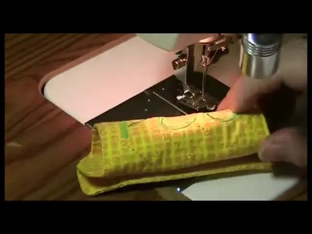The finished quilted luggage handle wrap is shaped into a cylinder as if wrapped around a suitcase handle, showing the green monogram on the yellow quilted background.