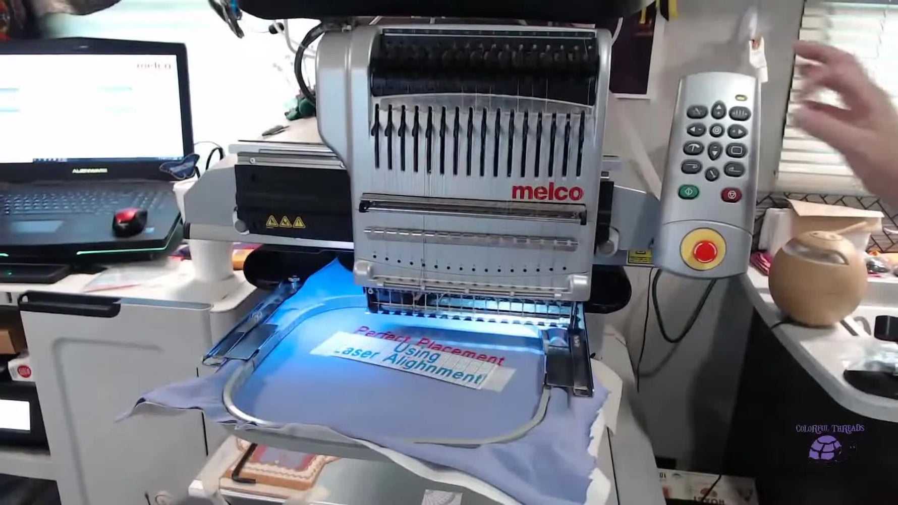 A close-up shows the Melco red laser dot landing precisely on a pencil-marked grid intersection on the printed alignment template.