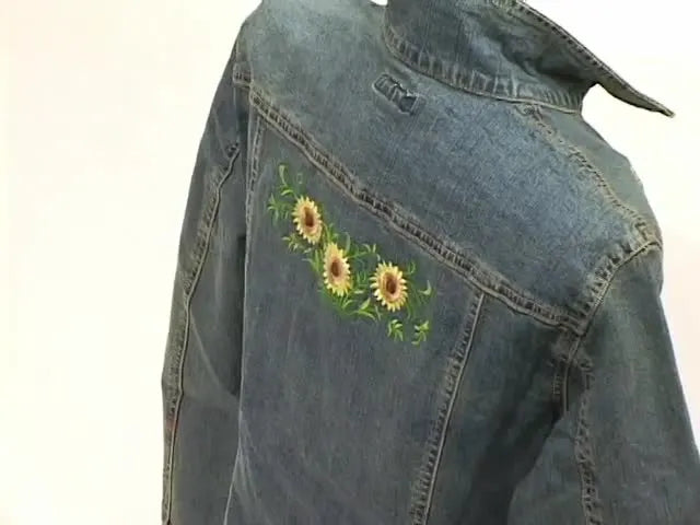 A close-up of a denim jacket back panel showing a large sunflower embroidery that highlights rayon sheen and coverage on heavy fabric.