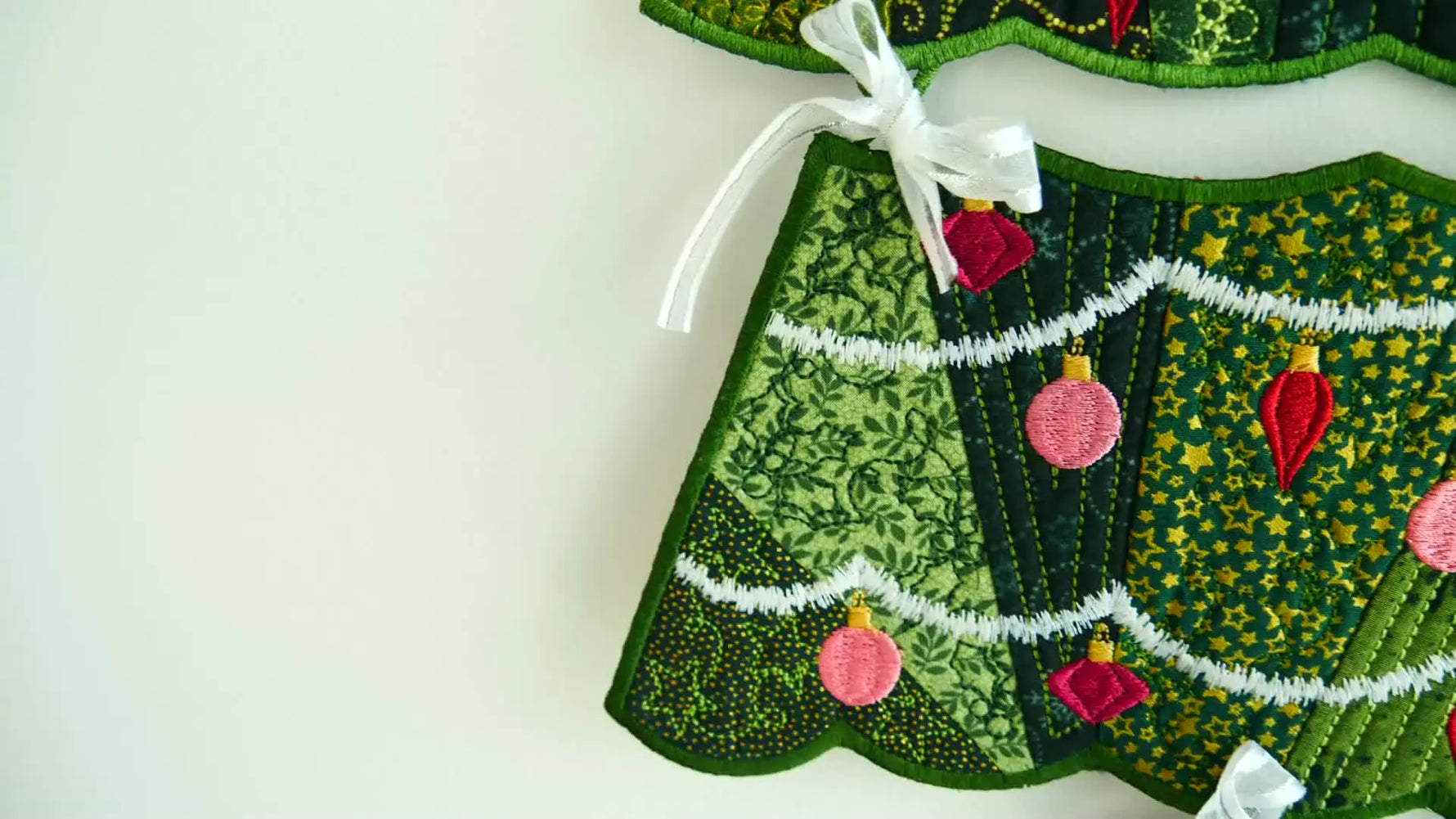 A finished in-the-hoop embroidered Christmas tree hanger with ribbon ties displayed as holiday decor.