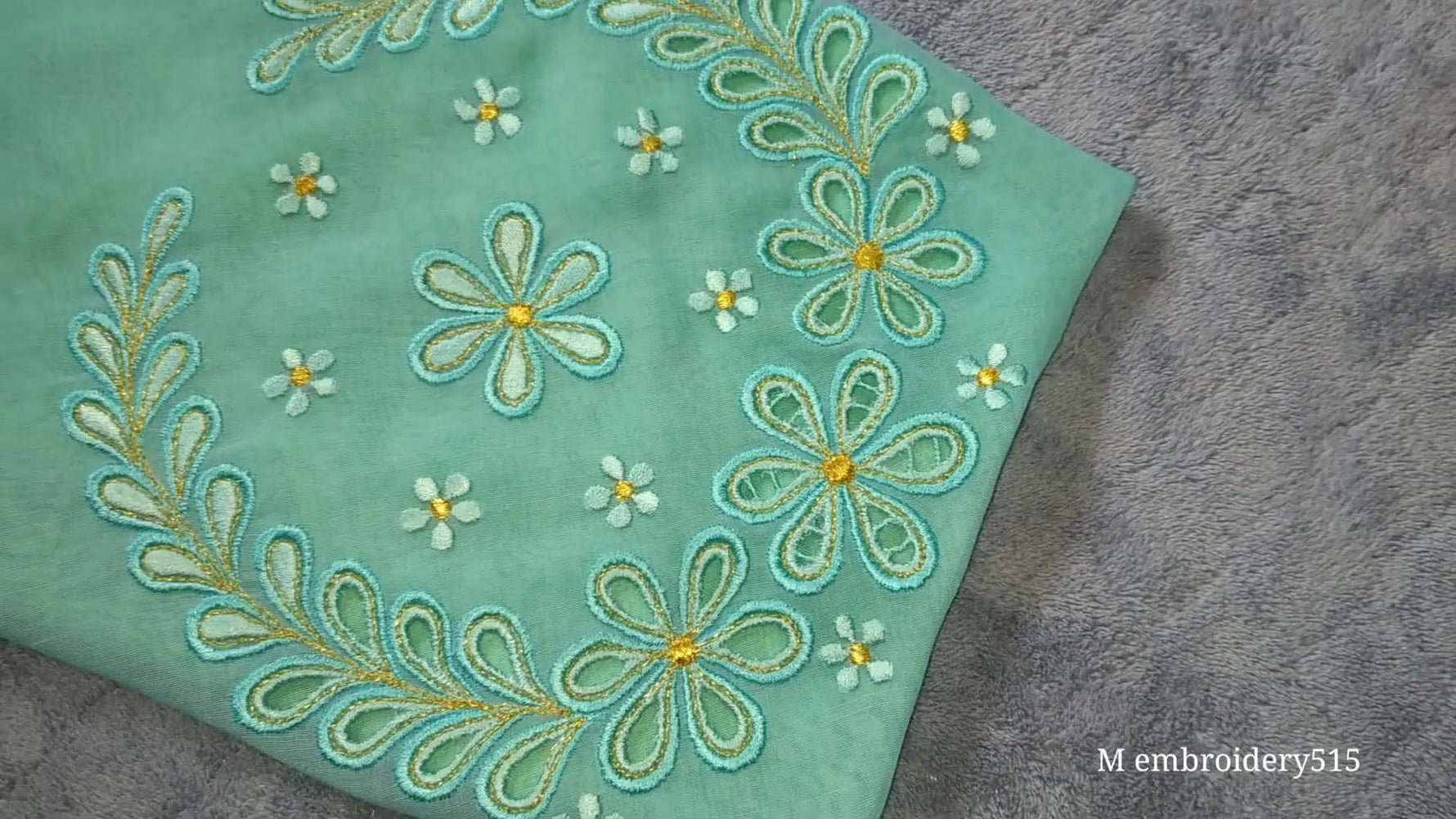 Close-up of a sleeve with intricate machine embroidery, featuring floral cutwork in teal and gold threads on sheer light green fabric.