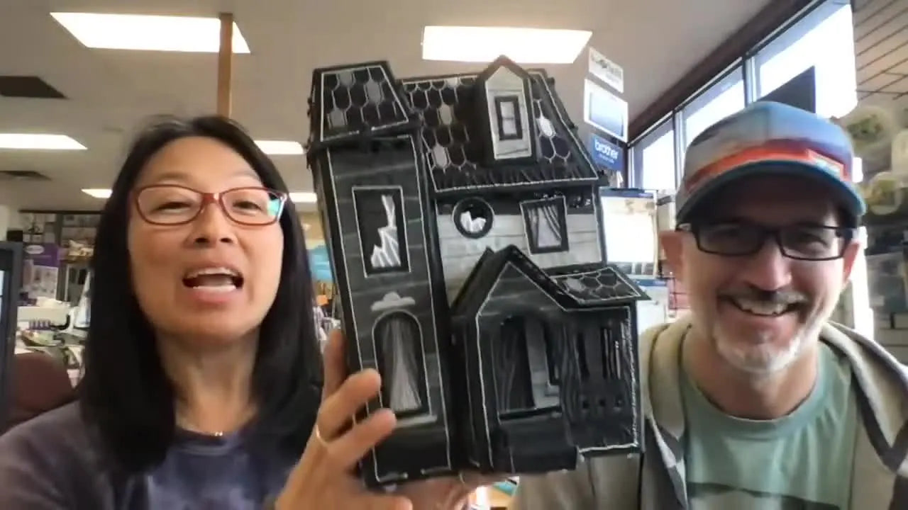 A close-up of the host holding the black OESD “Midnight Manor” freestanding lace haunted house, showing its dense structure and dramatic details.