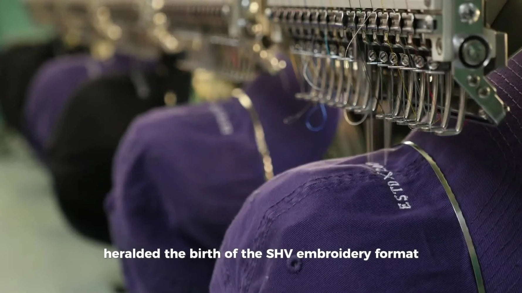 A row of industrial multi-needle embroidery machines stitching logos onto caps, showing real-world production where file compatibility and hooping speed matter.