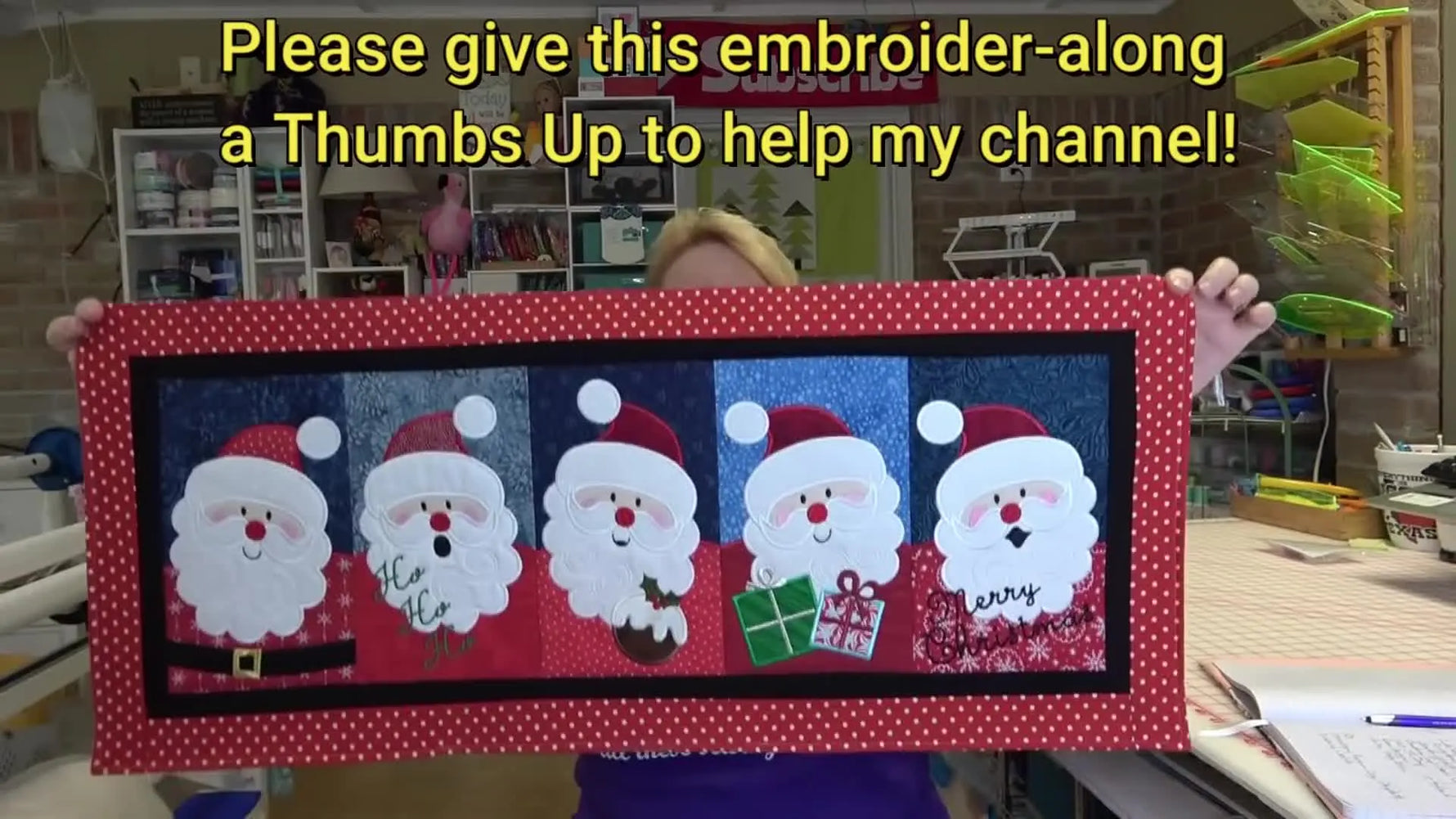 The fully assembled Santa table runner is held up to show all five applique blocks and the finished double border.