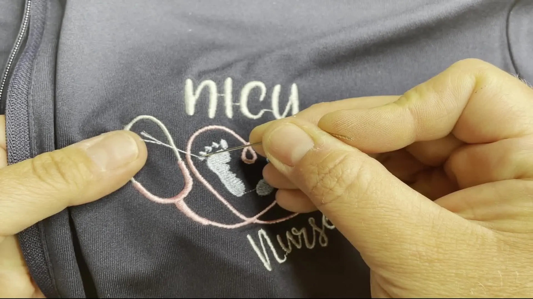 A close-up shows the Snag-Nab-It tip placed precisely at the base of a loose thread on an embroidered jacket, ready to pull the thread to the back.