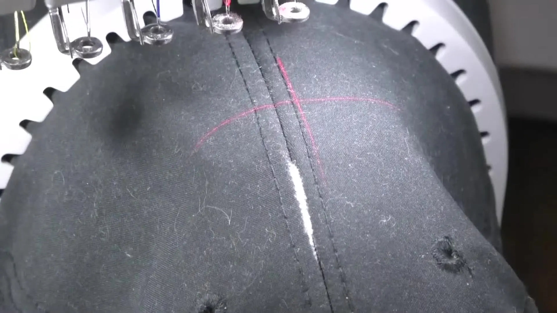 A red laser crosshair lands on the cap’s center seam, showing the exact alignment point before stitching on the Baby Lock Array.